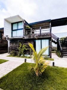 Contemporary two-story wooden house with lush greenery and palm plants.