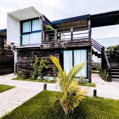 Contemporary two-story wooden house with lush greenery and palm plants.