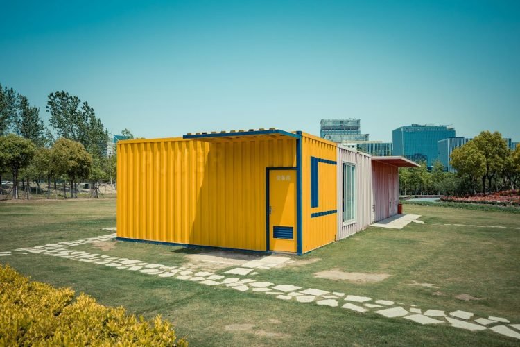 A bright yellow shipping container home on a green lawn.